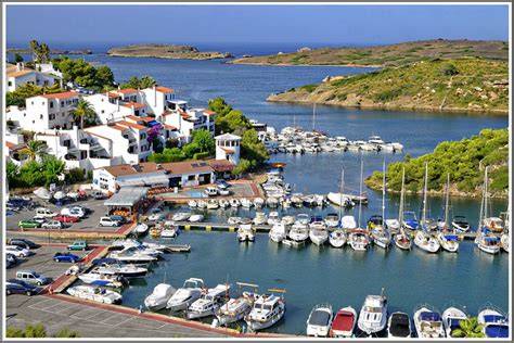 Aerial view of Port d'Addaia marina with white villas and moored yachts lining the sheltered inlet on Menorca's north coast