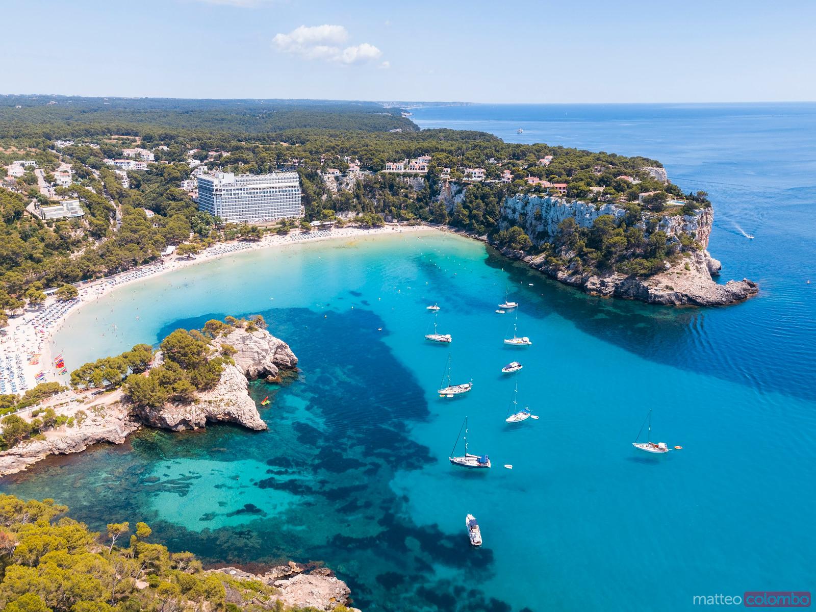 Aerial view of Cala Macarella and Cala Macarelleta beaches with sailing yachts anchored in turquoise water below limestone cliffs