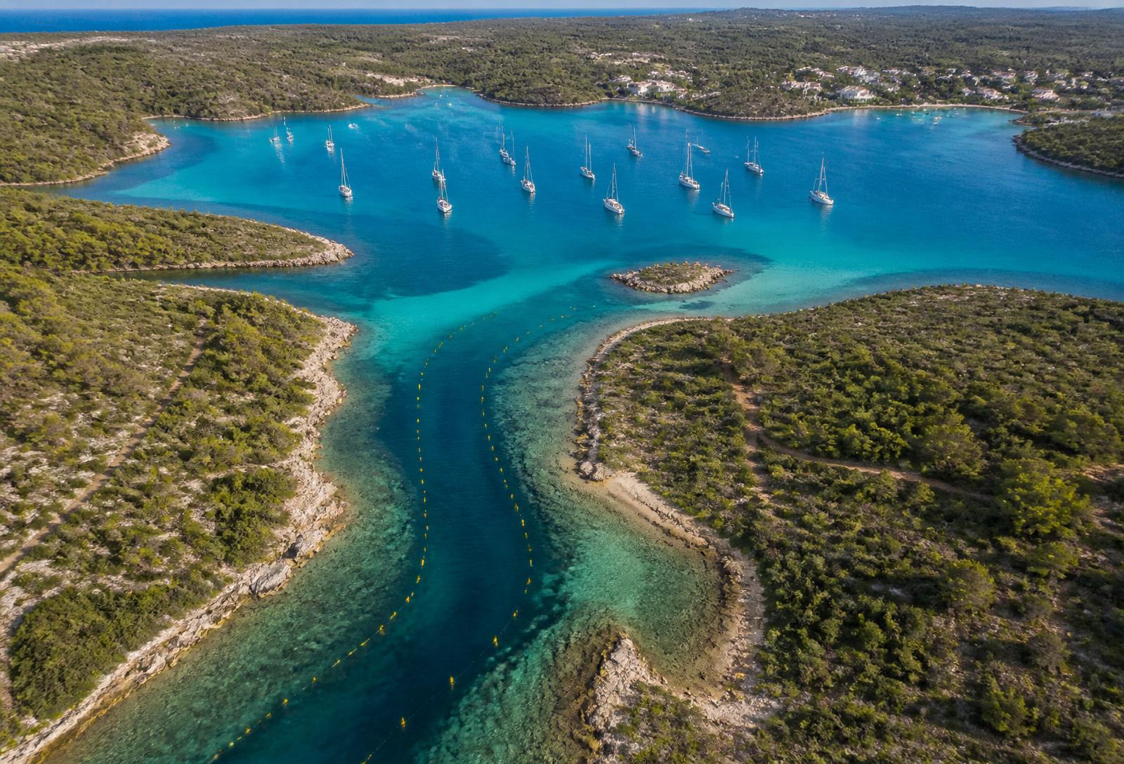 Aerial view of Addaia's buoyed channel opening into the calm inner lagoon with yachts at anchor